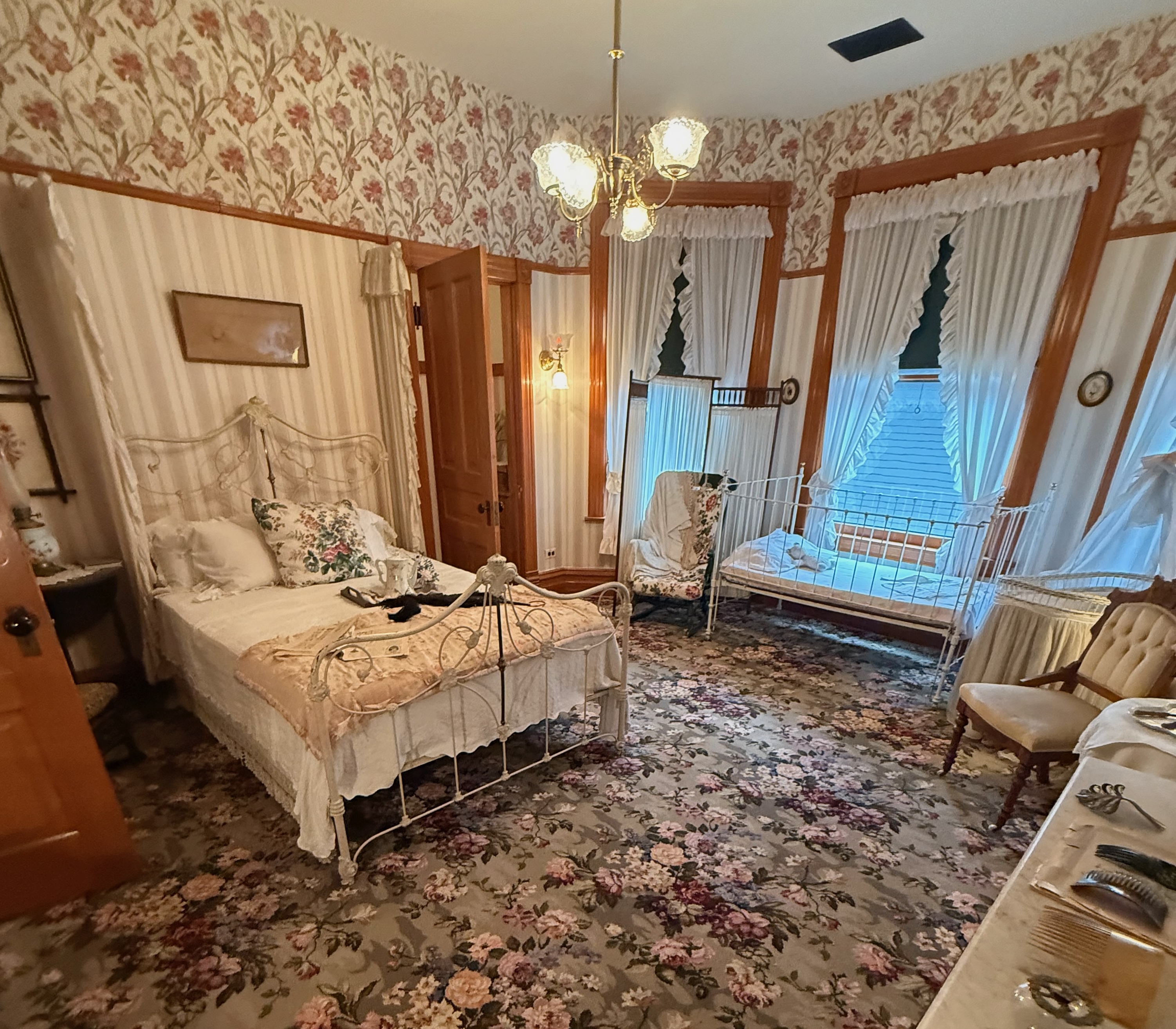 The Victorian bedroom where Ernest Hemingway was born, with a white iron bed, narrow crib, and floral carpet and wallpaper