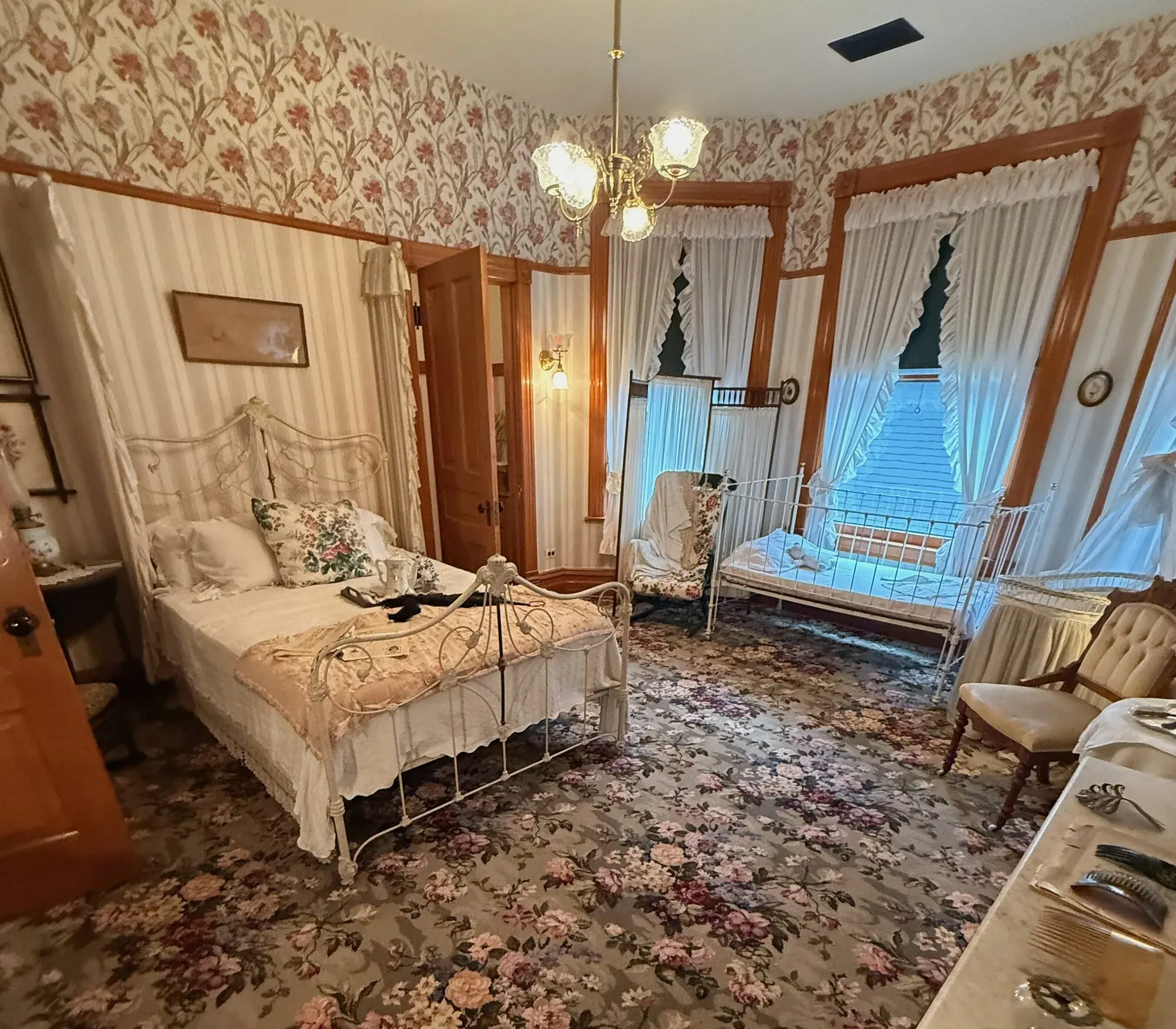 The Victorian bedroom where Ernest Hemingway was born, with a white iron bed, narrow crib, and floral carpet and wallpaper