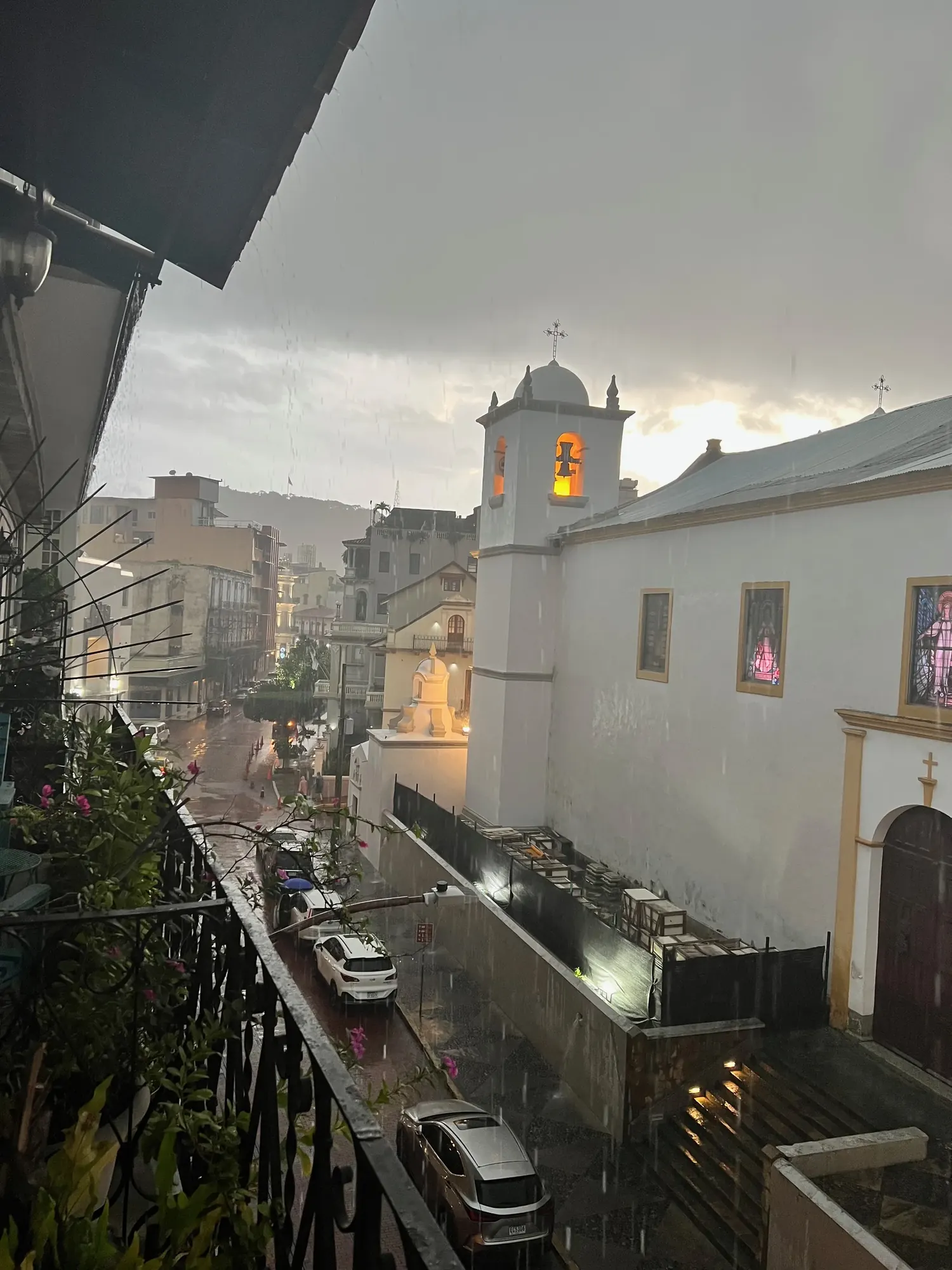 Rain falling across a Casco Viejo street at dusk, a lit bell tower visible through the storm